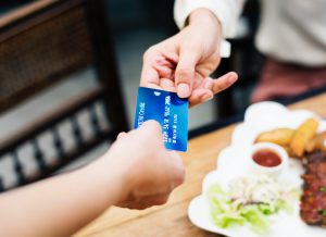 person handing blue credit card to server at restaurant over plate